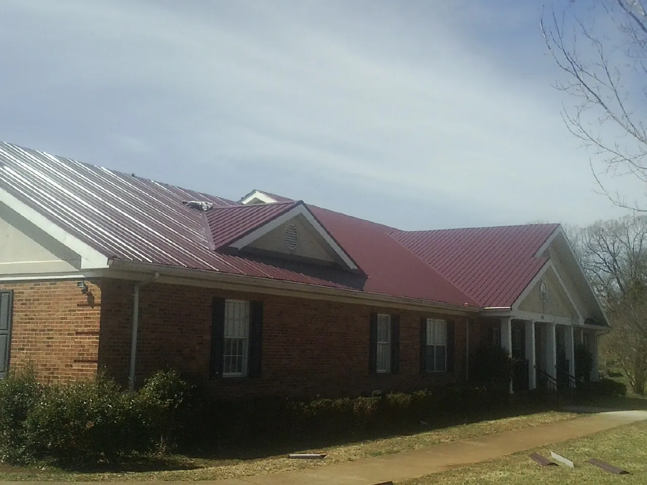 Red metal roof with gabled entries on a long brick building, from a Hail Damage Roof Repair job in Drums