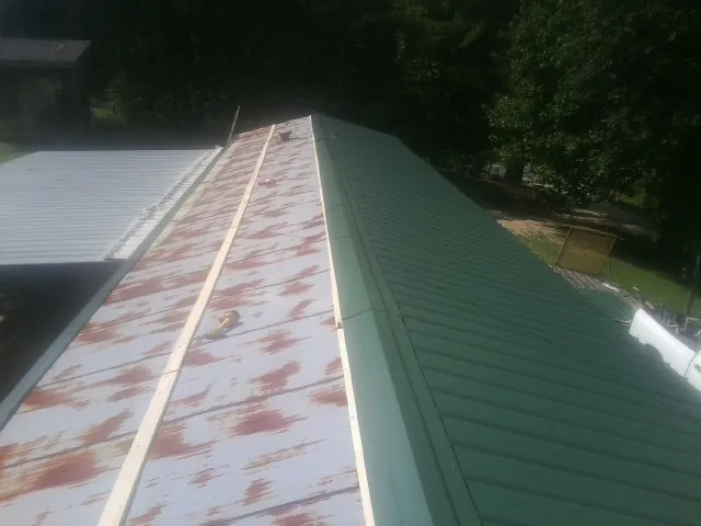 Old rusted panels beside newly installed green metal roofing — Wind Damage Roof Repair by Roofing Brothers in Drums