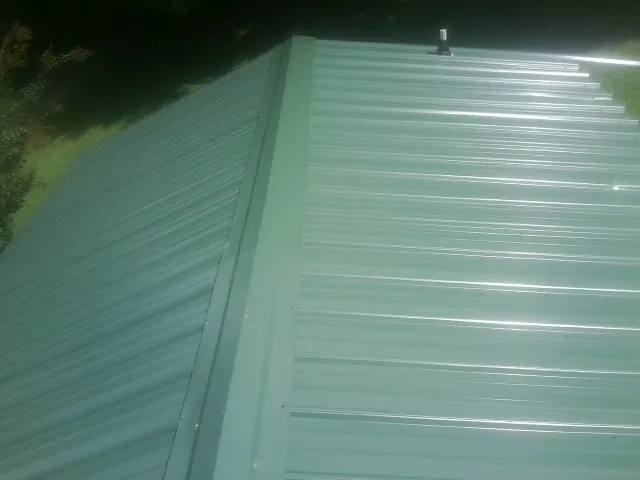 New green metal panels meeting at the ridge of a roof — Flat Roof Repair work by our crew in Drums