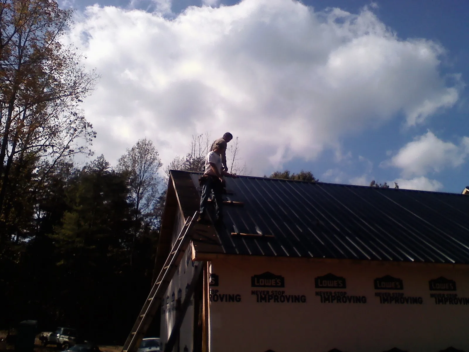 Roofer fastening dark metal panels high against a cloudy sky, from a Roof Inspection job in Drums